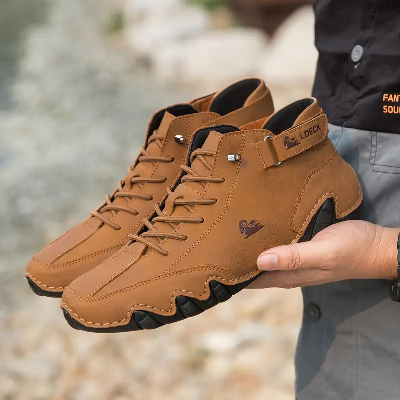 Person holding a pair of brown leather hiking boots outdoors.