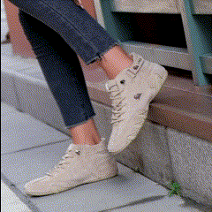 Person wearing beige high-top sneakers and jeans sitting on a ledge.
