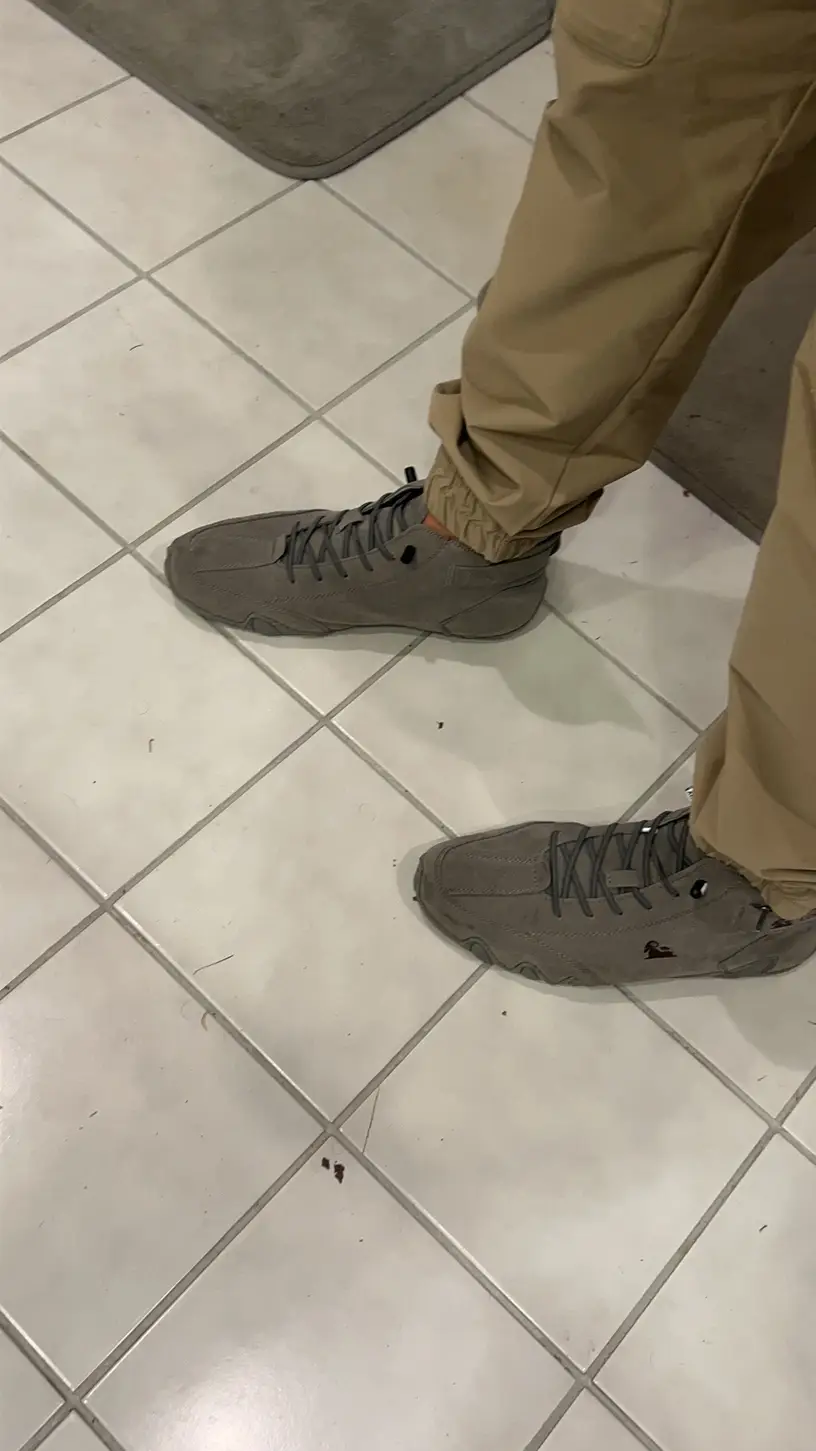 Person wearing gray sneakers and khaki pants on a tiled floor.