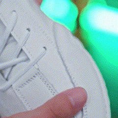 Close-up of a hand holding a white sneaker with green lights in the background.