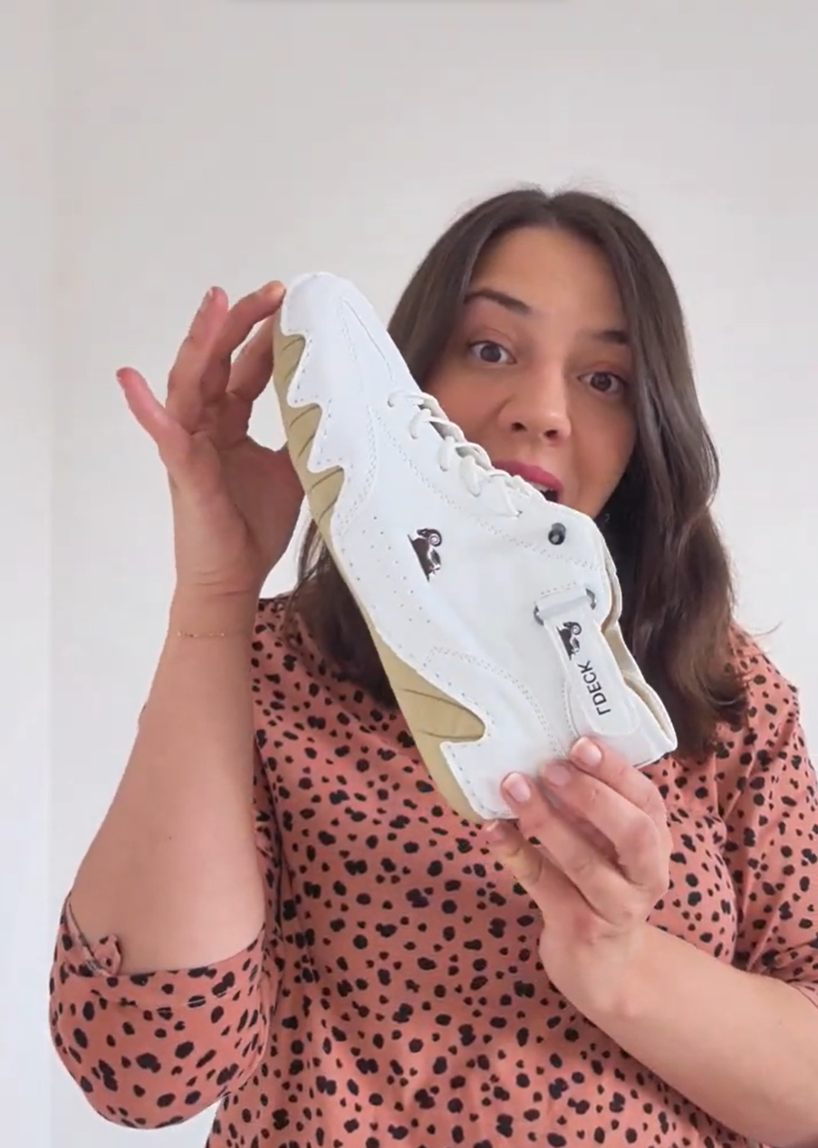 Person holding a white sneaker with beige sole, wearing a polka dot shirt.