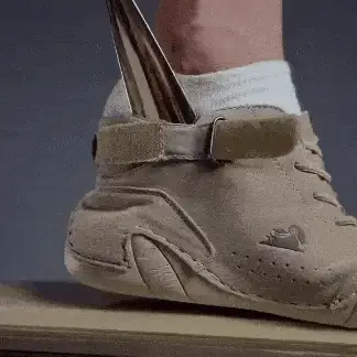 A foot in a beige shoe with a knife piercing through the sole.