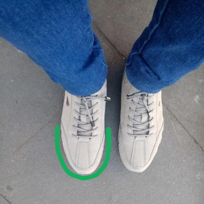 Person wearing beige sneakers and blue jeans standing on a gray pavement.