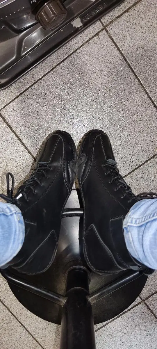 Person wearing black boots and jeans, sitting on a stool with tiled floor.