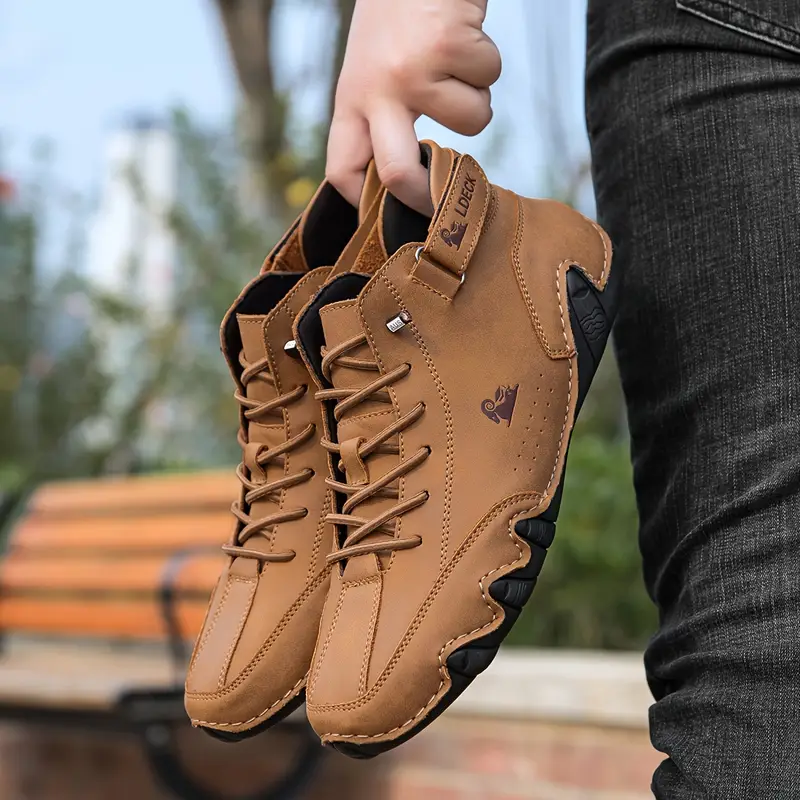 Person holding a pair of brown leather shoes outdoors.
