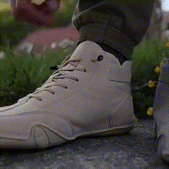 Person tying beige high-top sneakers outdoors on a stone surface.