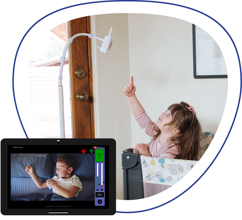 A young girl in a playpen points up at a baby monitor, with a tablet showing another child sleeping.