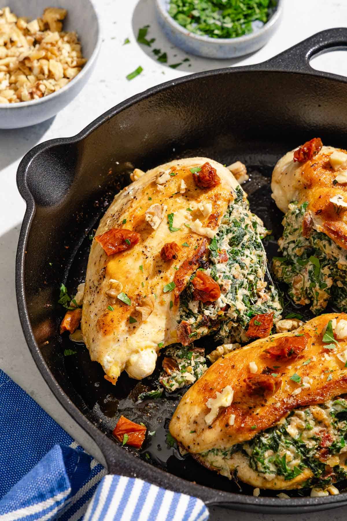 Close-up of spinach and sun-dried tomato stuffed chicken breasts searing in a cast-iron skillet.