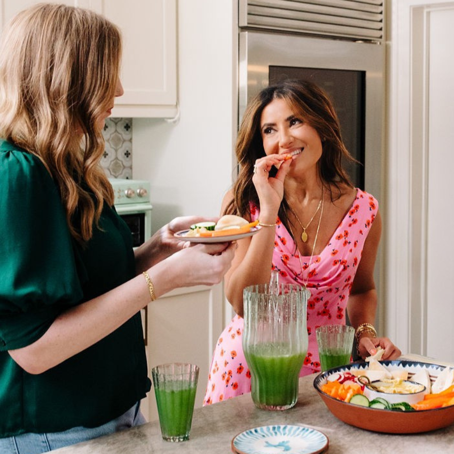 Two people in a kitchen with green drinks and a platter of vegetables.