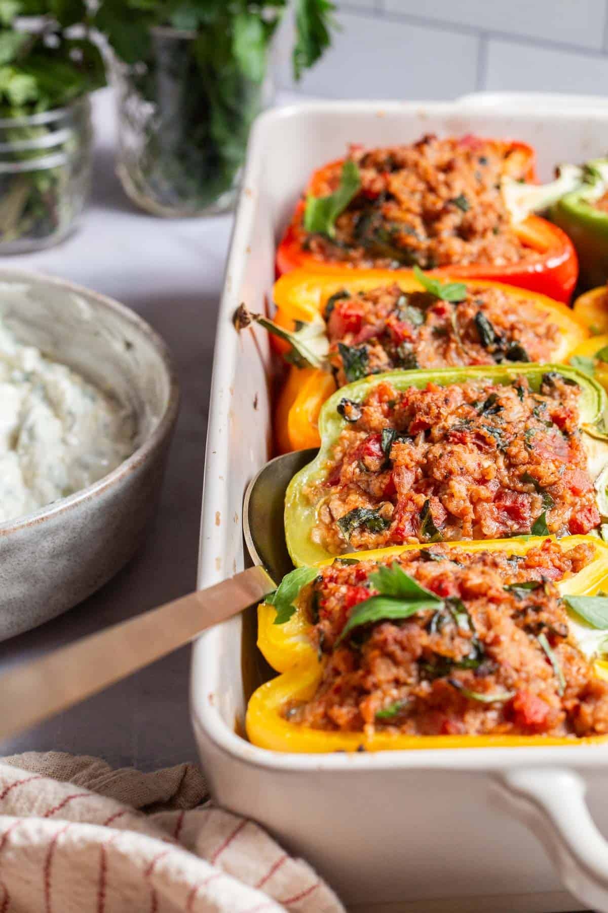 Close-up of colorful stuffed bell peppers in a white baking dish with a serving spoon.