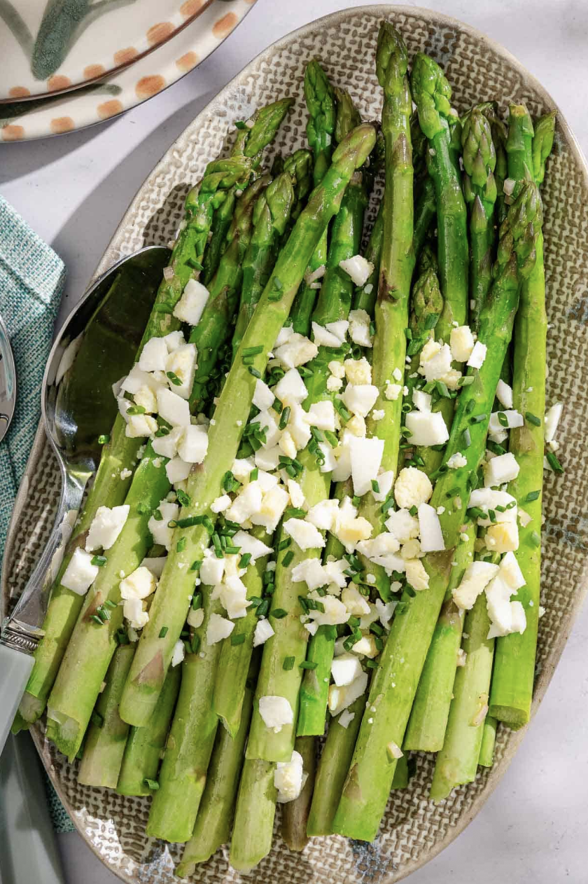 Plate of asparagus topped with chopped eggs and herbs.
