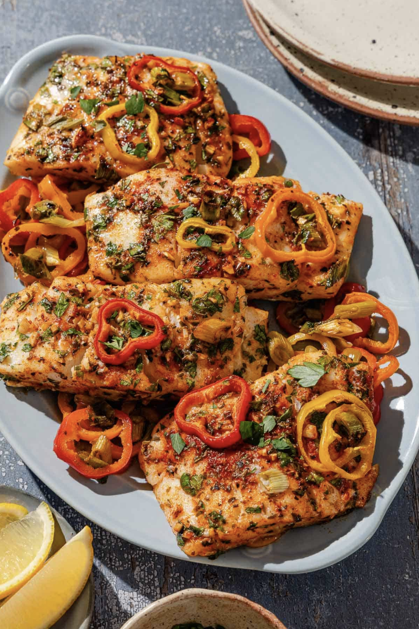 Grilled fish fillets with herbs and sliced bell peppers on a plate.