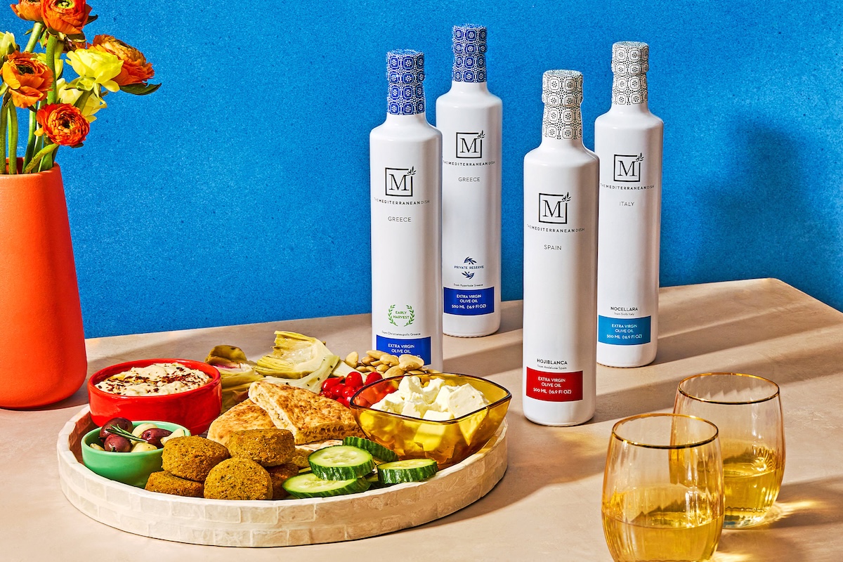 A platter of Mediterranean food, including falafel and dips, next to bottles of olive oil and flowers.