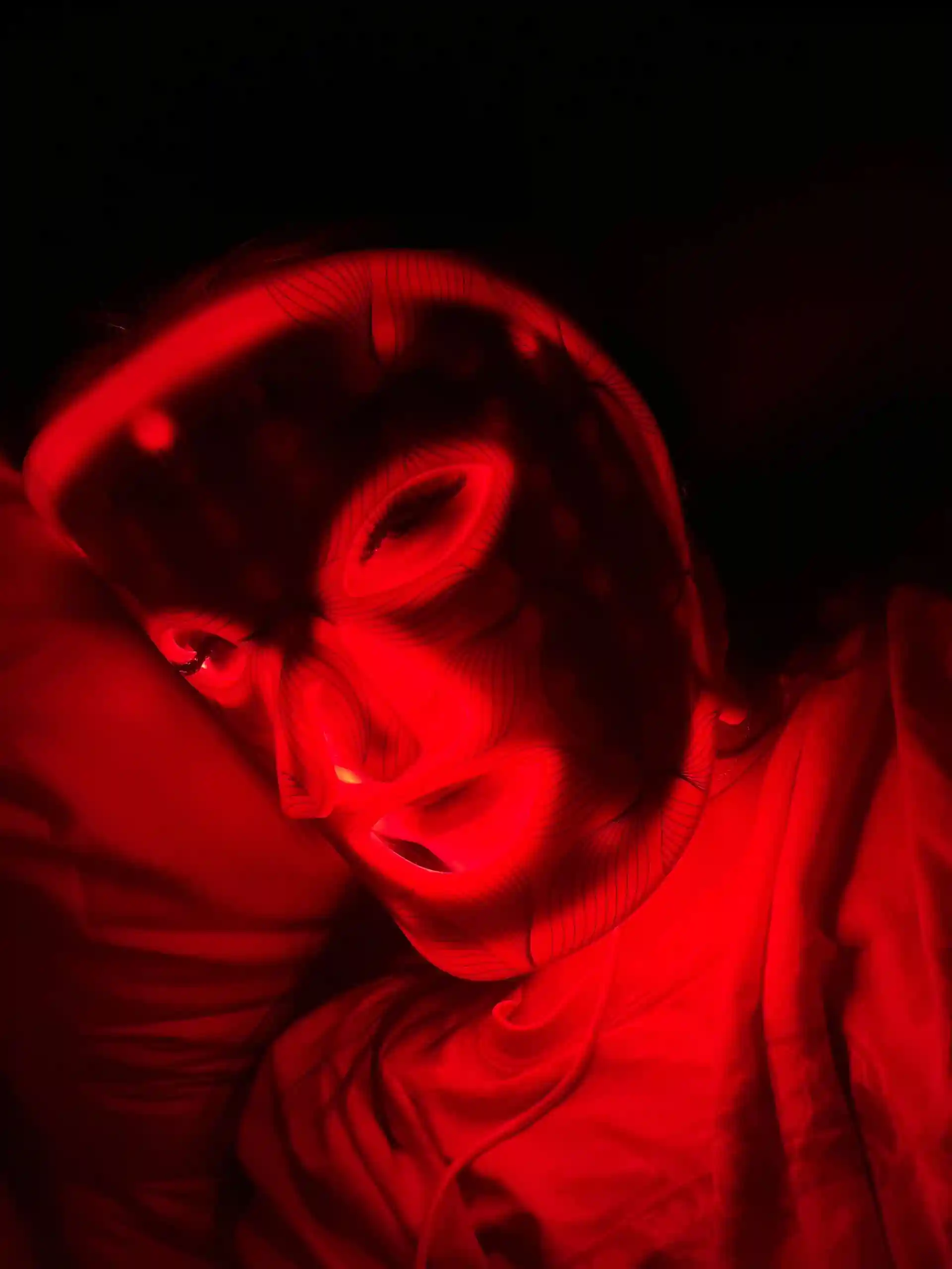 Person wearing a glowing red LED face mask in a dark setting.