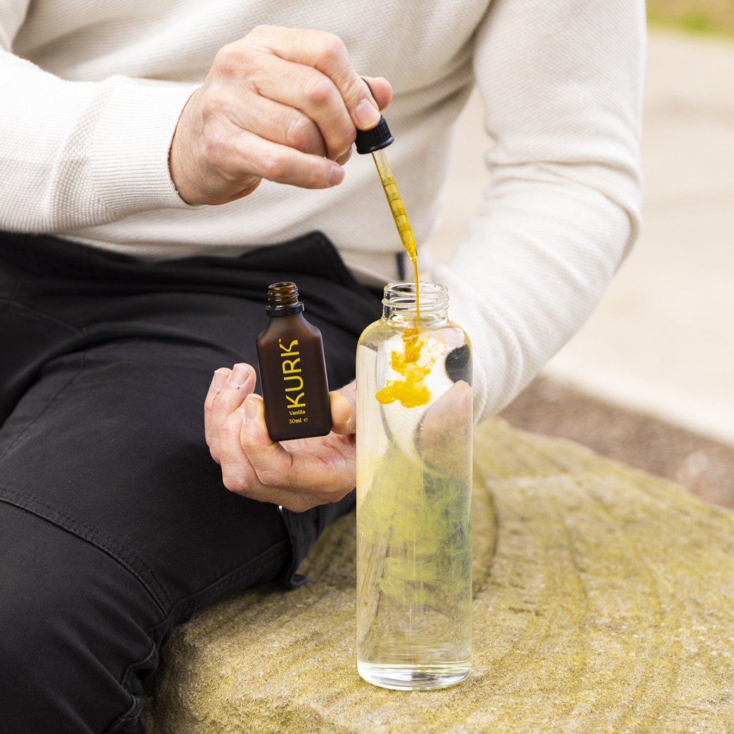 A person adds yellow liquid from a dropper into a clear bottle filled with water.