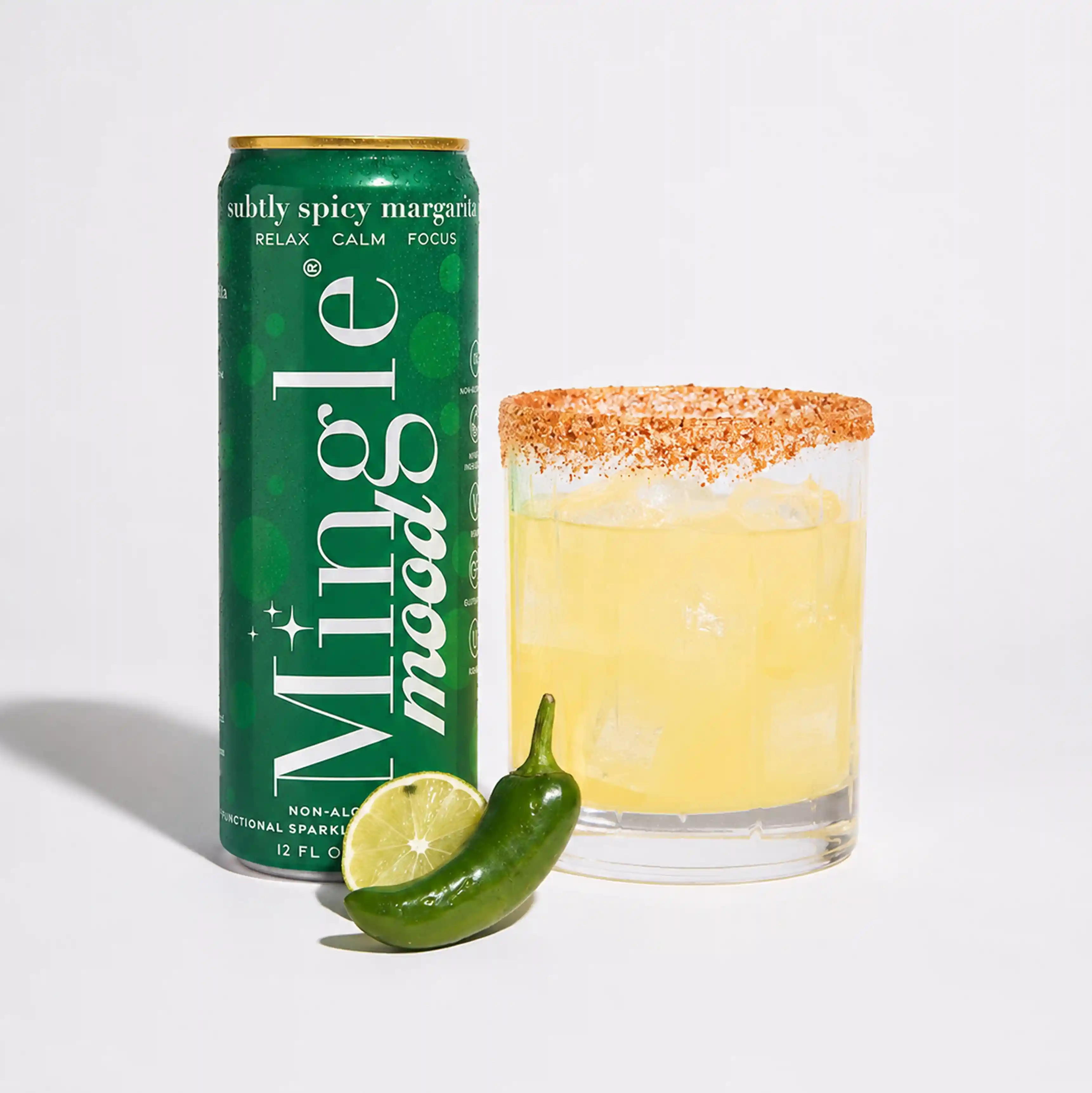 A can of Mingle non-alcoholic spicy margarita next to a spiced-rim glass, a lime, and a jalapeño.