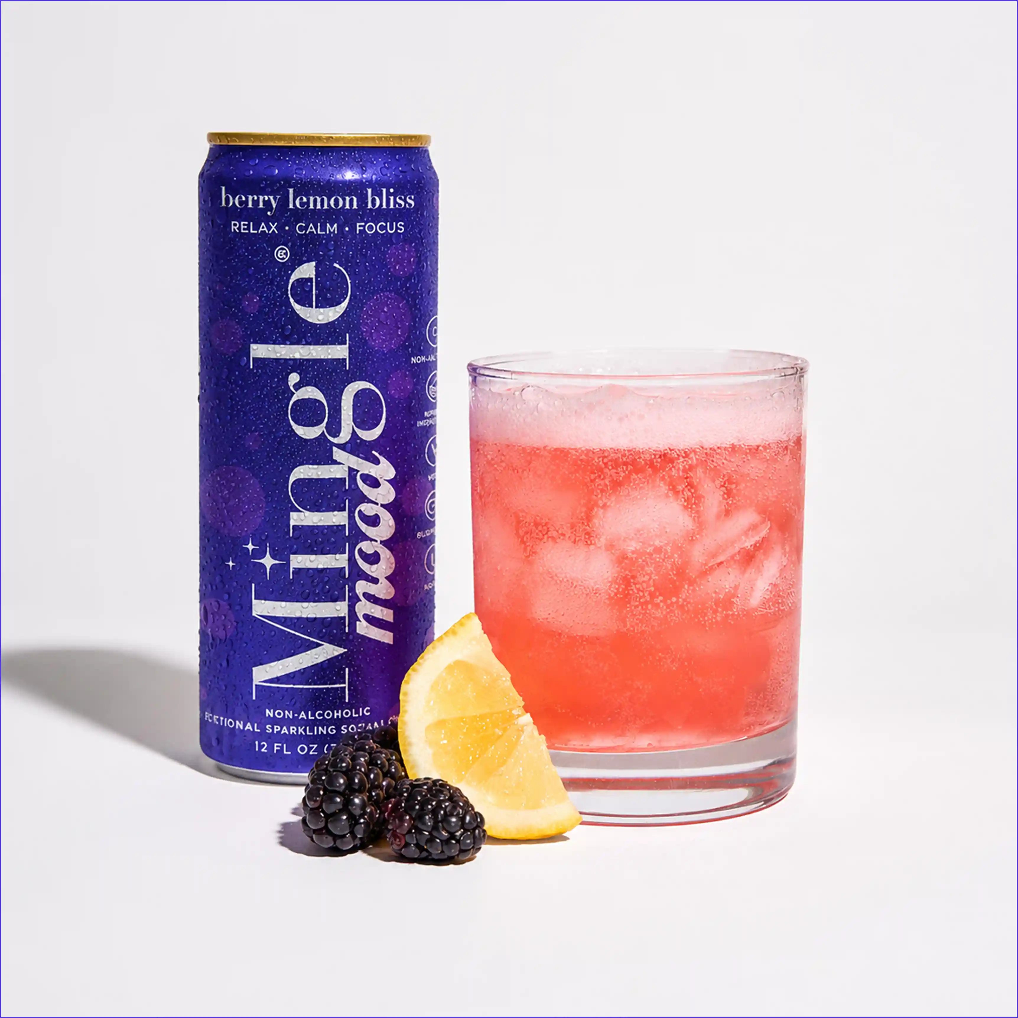 A can of Mingle mood drink next to a glass of a pink beverage, with blackberries and lemon.