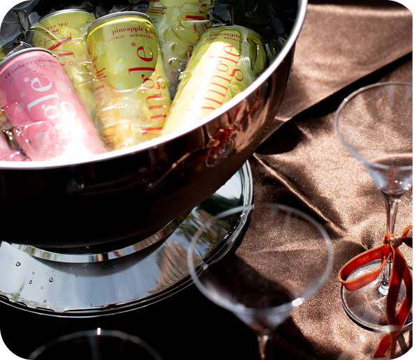 Cans of sparkling juice in an ice bucket on a table next to empty martini glasses.