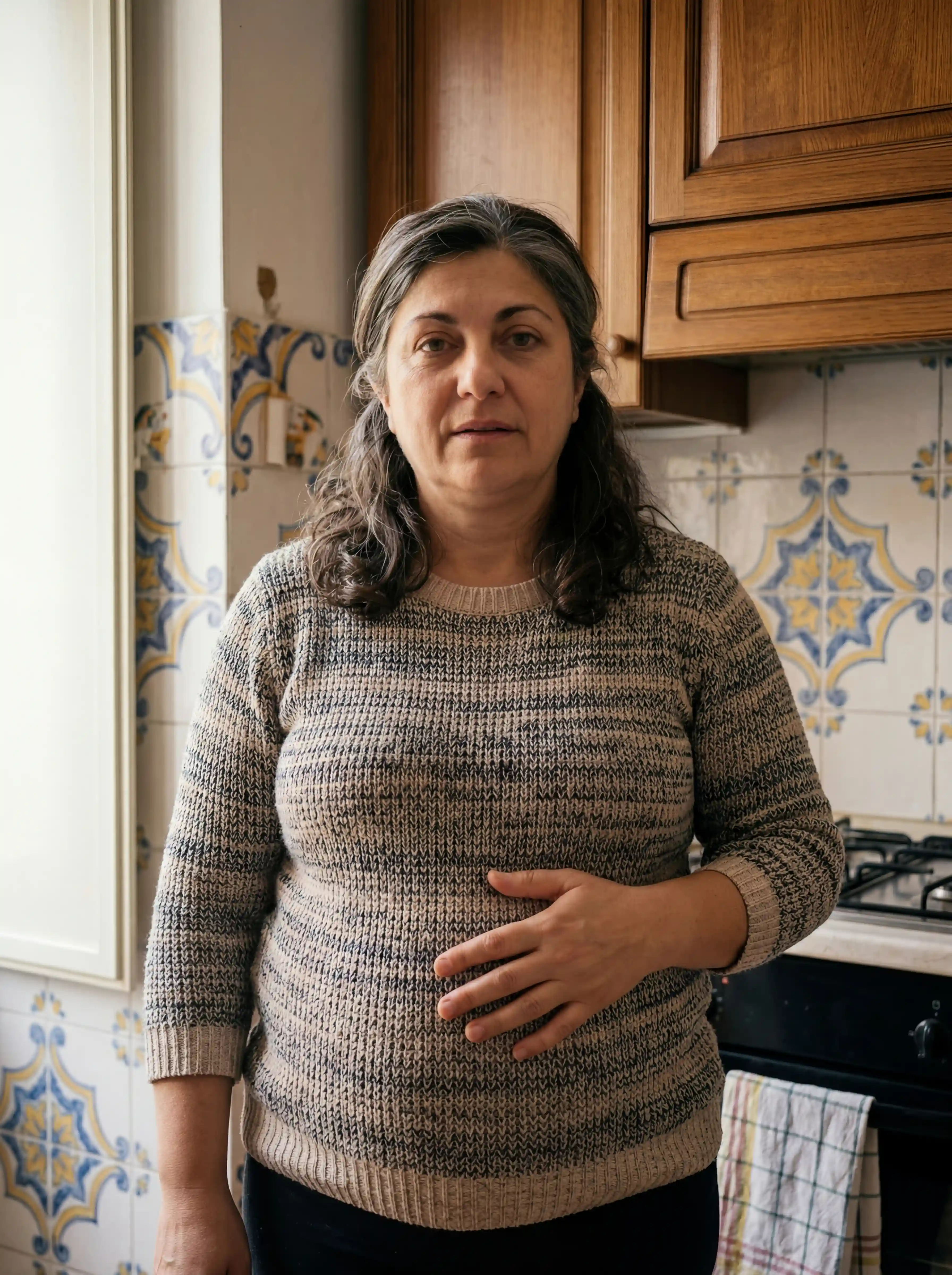 A woman with graying hair in a sweater stands in a kitchen looking at the camera.