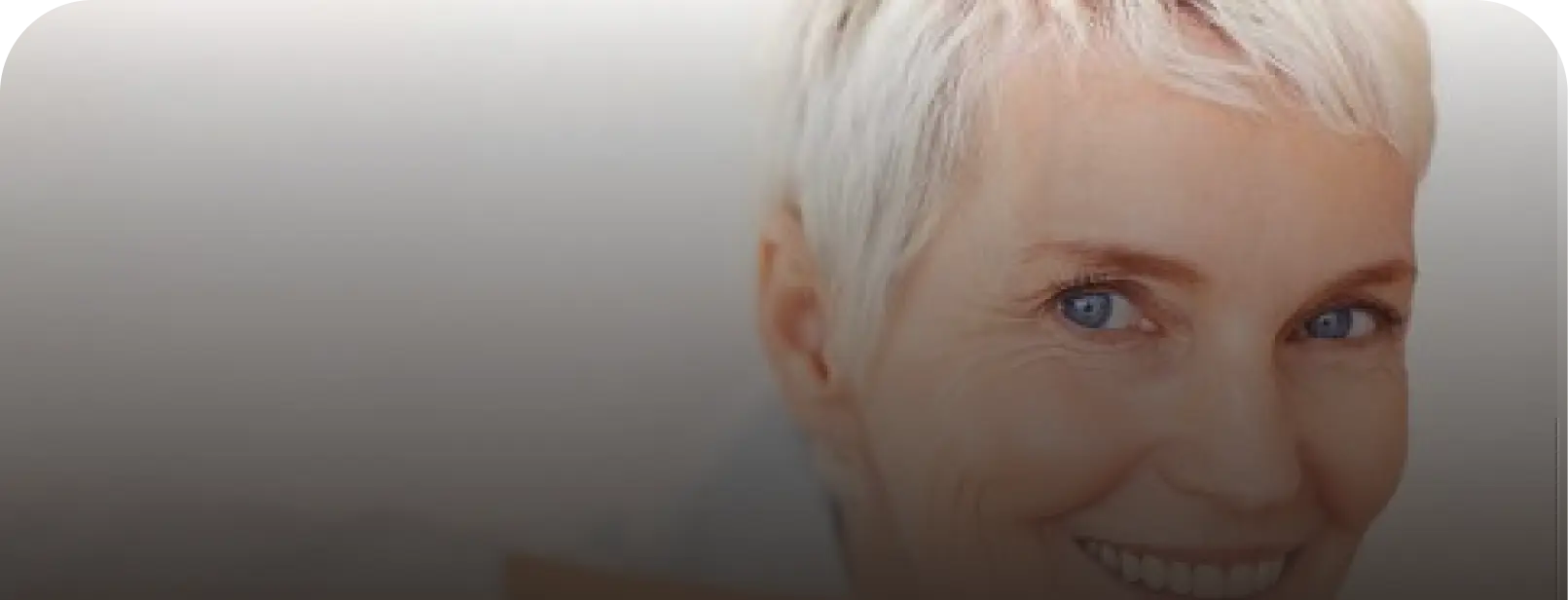 A close-up of a smiling older woman with short white hair and blue eyes.