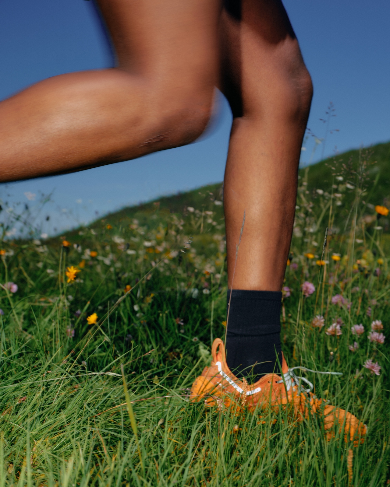 Close-up of a person running in orange shoes through a grassy field with wildflowers.