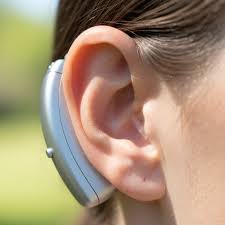 A close-up of a silver hearing device worn behind a person's ear.