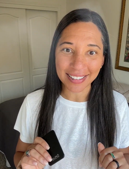 A smiling woman in a white t-shirt holds up a small, black, rectangular object with 'AURO' on it.