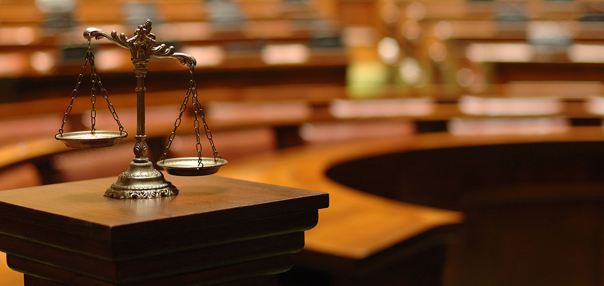 A set of Scales of Justice sits on a wooden podium inside a courtroom.