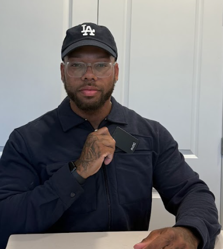 A man in a baseball cap and glasses places a black card into his jacket's chest pocket.