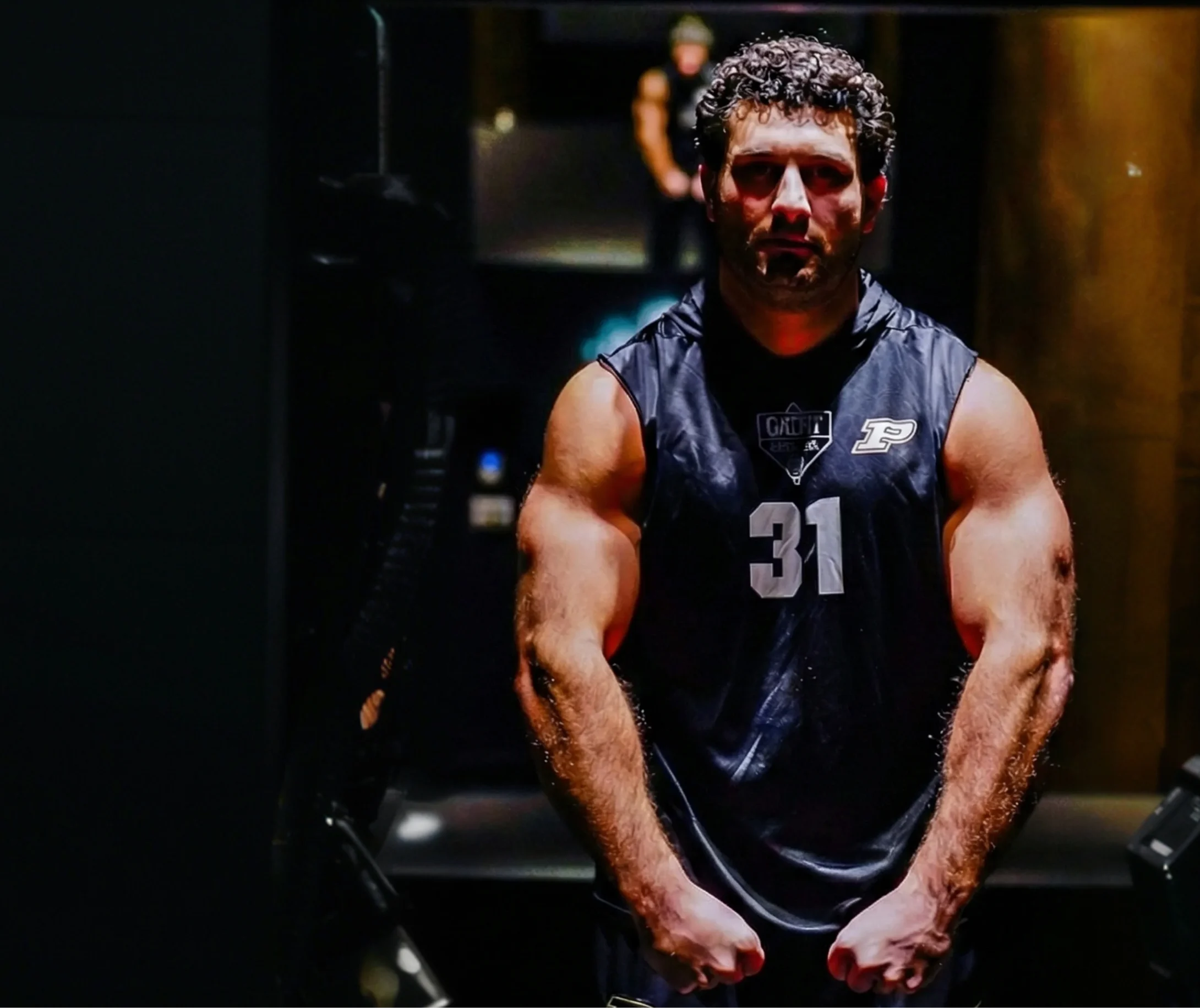 A muscular man in a black sleeveless Purdue jersey with the number 31 flexes his arms.