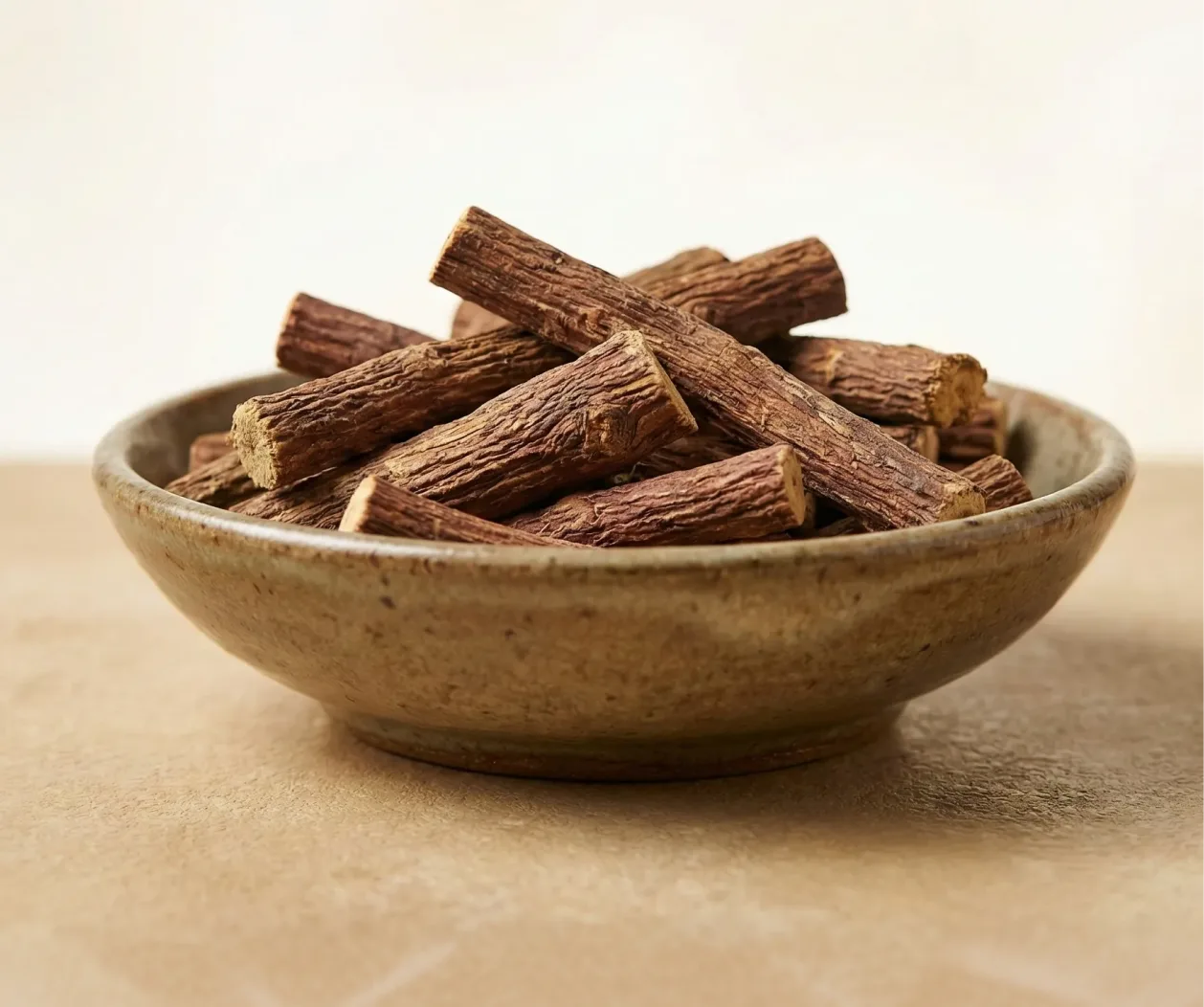 A rustic brown bowl filled with pieces of dried licorice root.