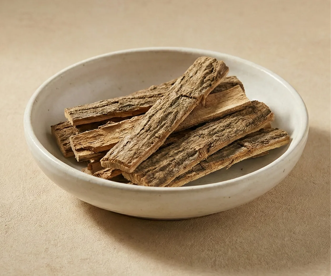 A white bowl filled with pieces of dried tree bark on a beige surface.