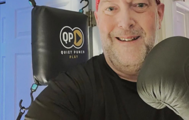 Person smiling with boxing glove in front of Quiet Punch punching bag.