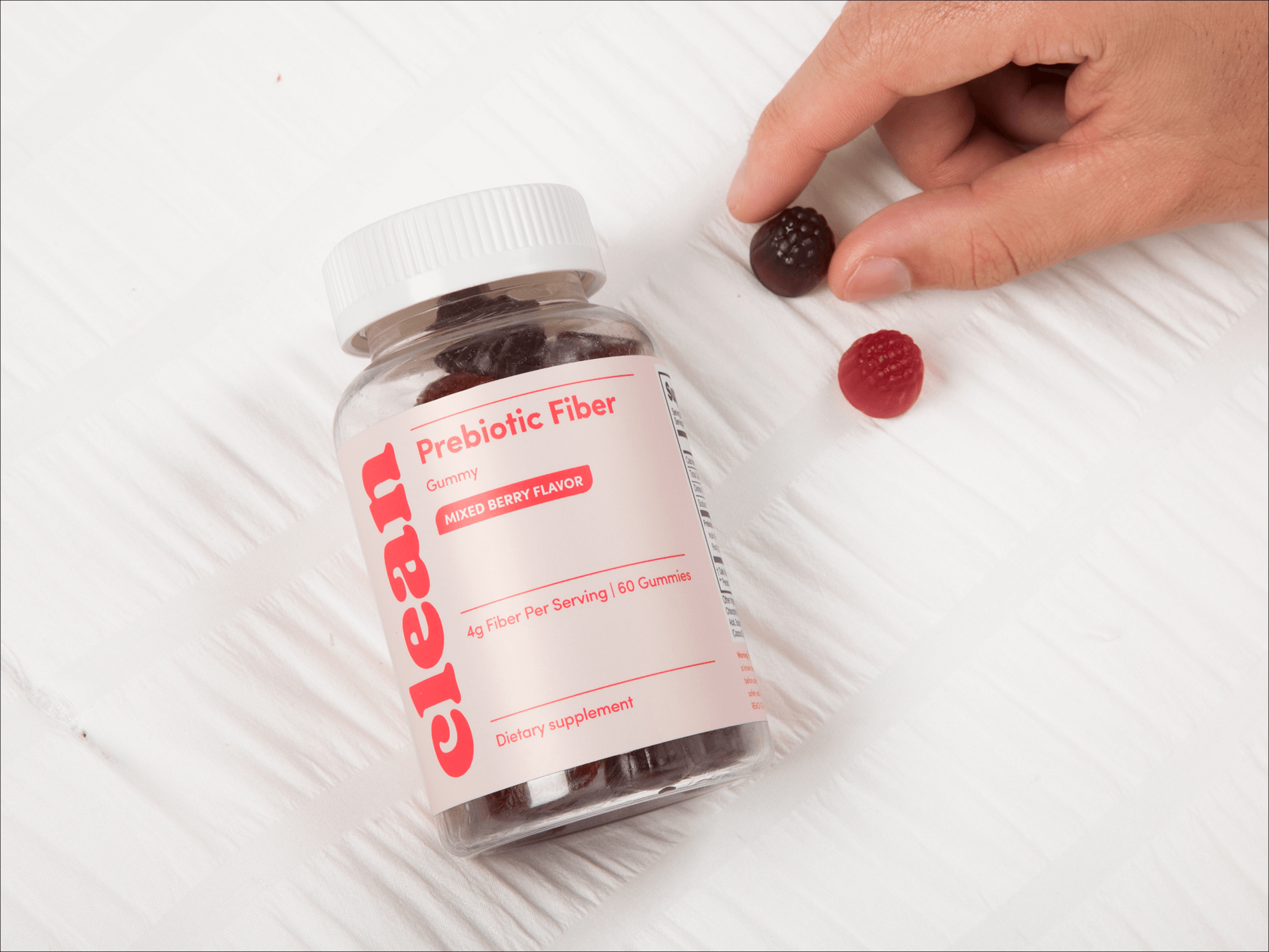 Bottle of prebiotic fiber gummies labeled 'clean,' with berry-shaped gummies nearby.