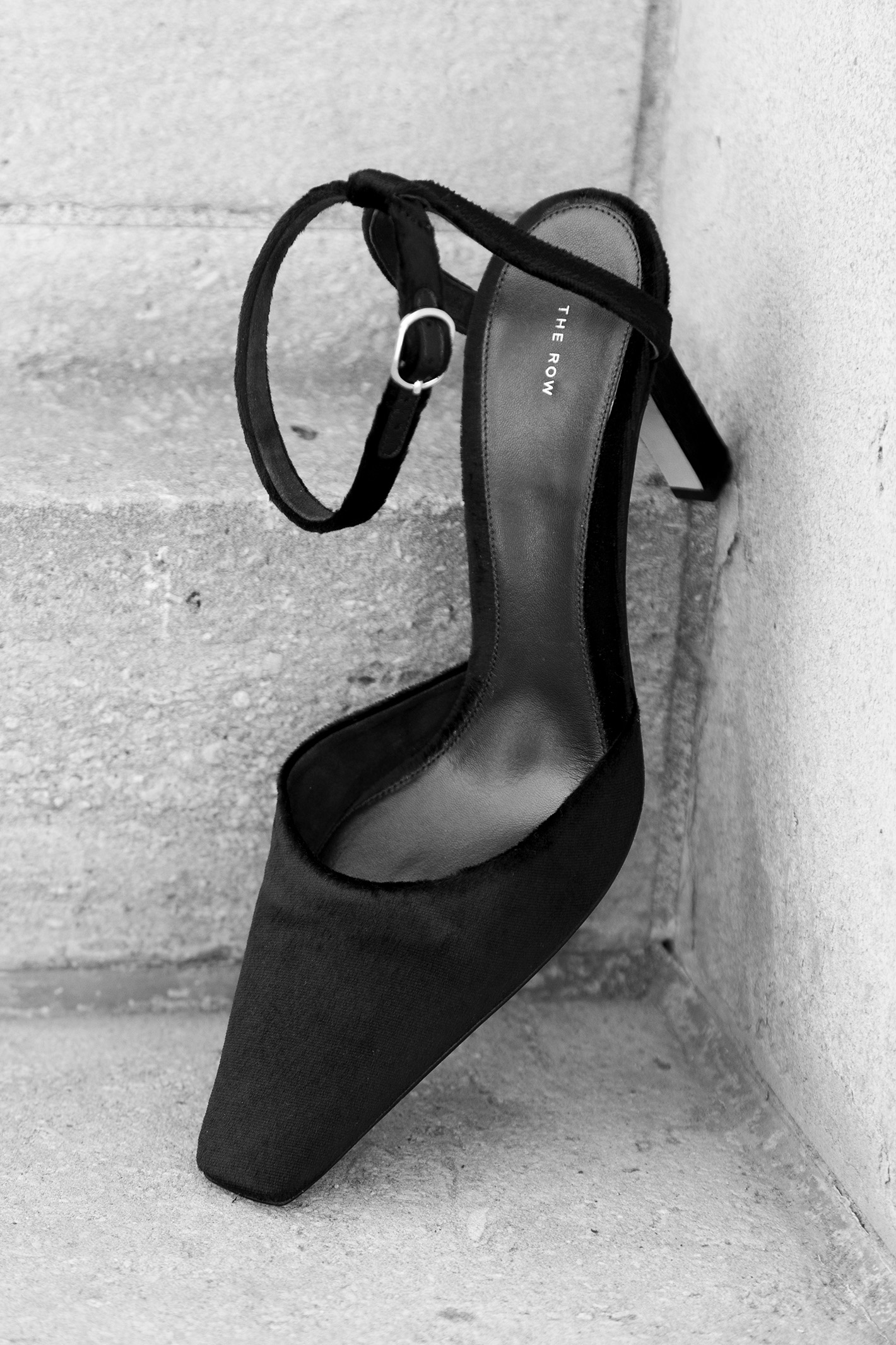Black high-heeled shoe with ankle strap on concrete steps.
