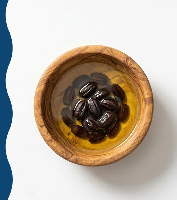 An overhead view of a wooden bowl with dark seeds soaking in a golden liquid against a white background.
