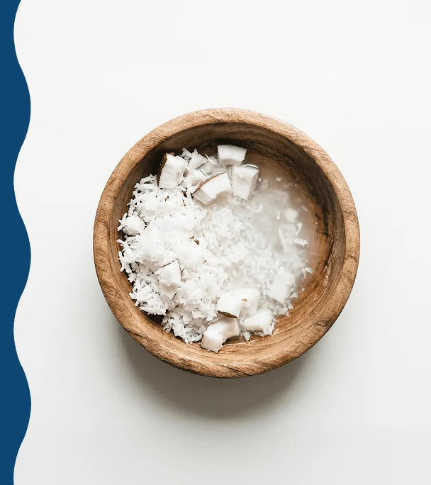 An overhead shot of a wooden bowl filled with shredded and cubed coconut in liquid.