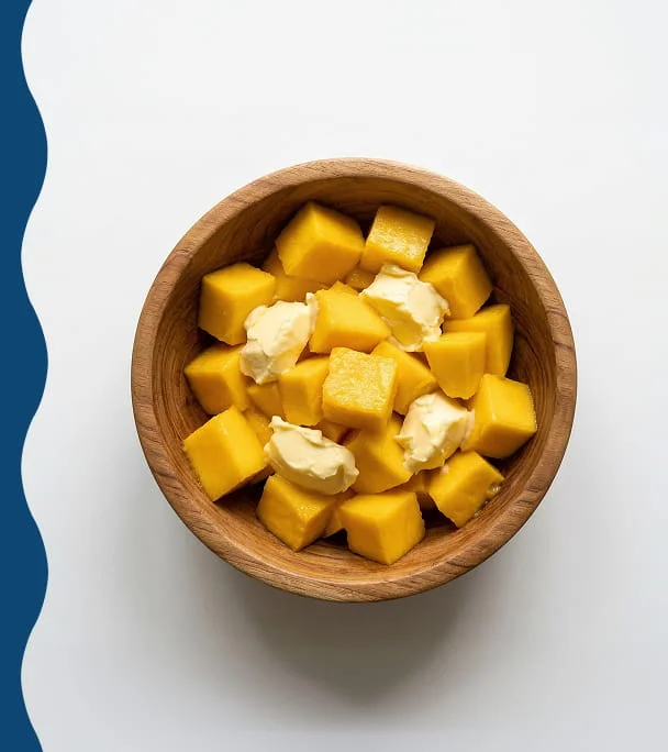 A wooden bowl filled with cubes of yellow fruit and dollops of a creamy substance.