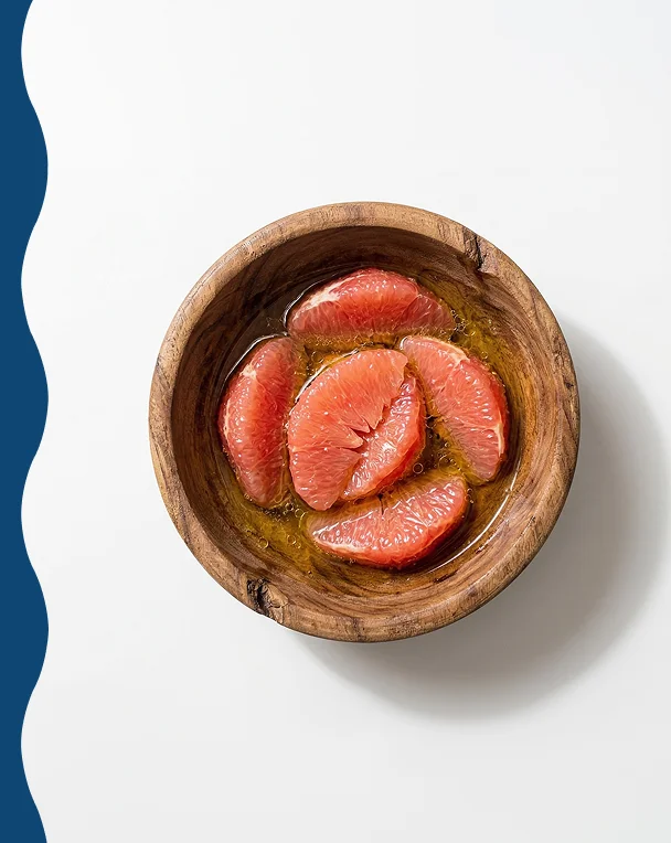 An overhead shot of pink grapefruit segments in a liquid, served in a rustic wooden bowl.
