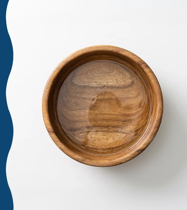 An overhead view of a wooden bowl filled with water on a white background with a blue wave element.