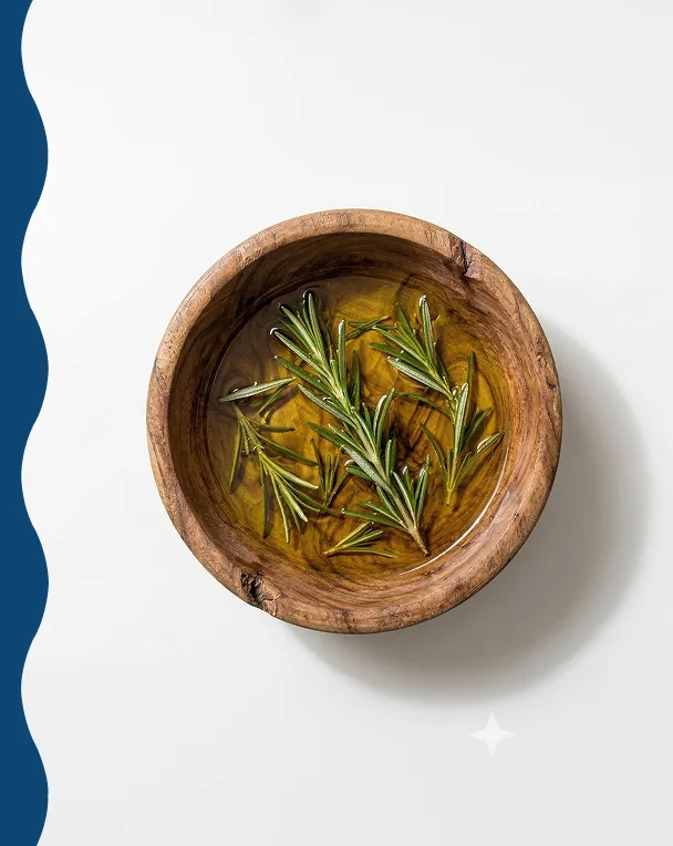 An overhead view of a wooden bowl filled with oil and sprigs of rosemary.