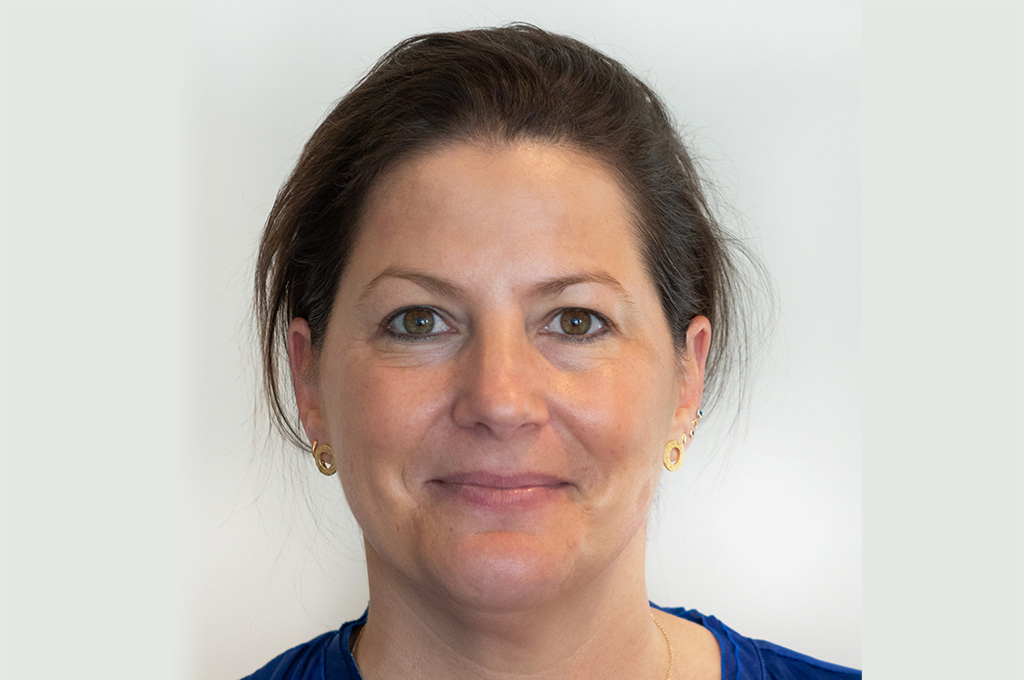 A person with a blue shirt and gold earrings smiling at the camera.