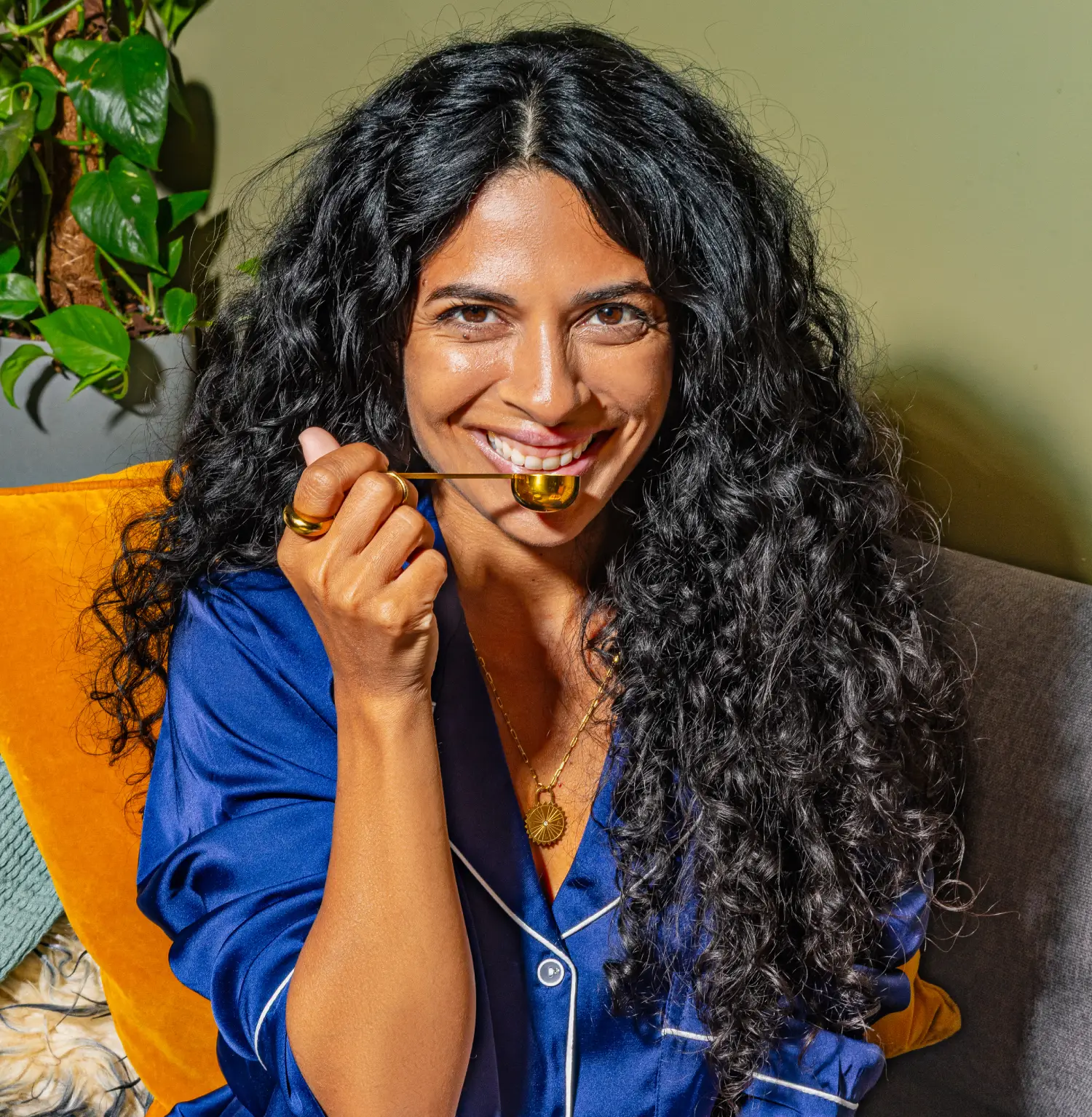 Woman in blue pajamas smiling with a gold spoon in her mouth.