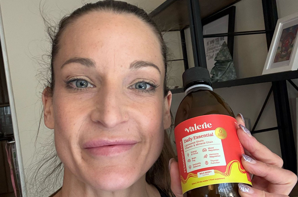Person holding a bottle labeled 'Valerie Daily Essential' in front of shelves.