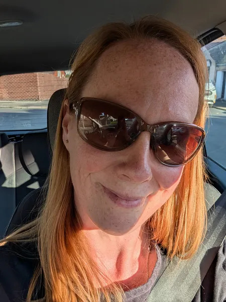 Person with sunglasses sitting in a car, smiling at the camera.