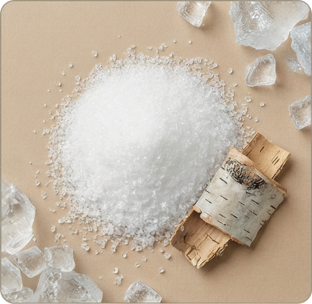 An overhead shot of white crystalline granules, larger clear crystals, and pieces of birch bark on a beige surface.