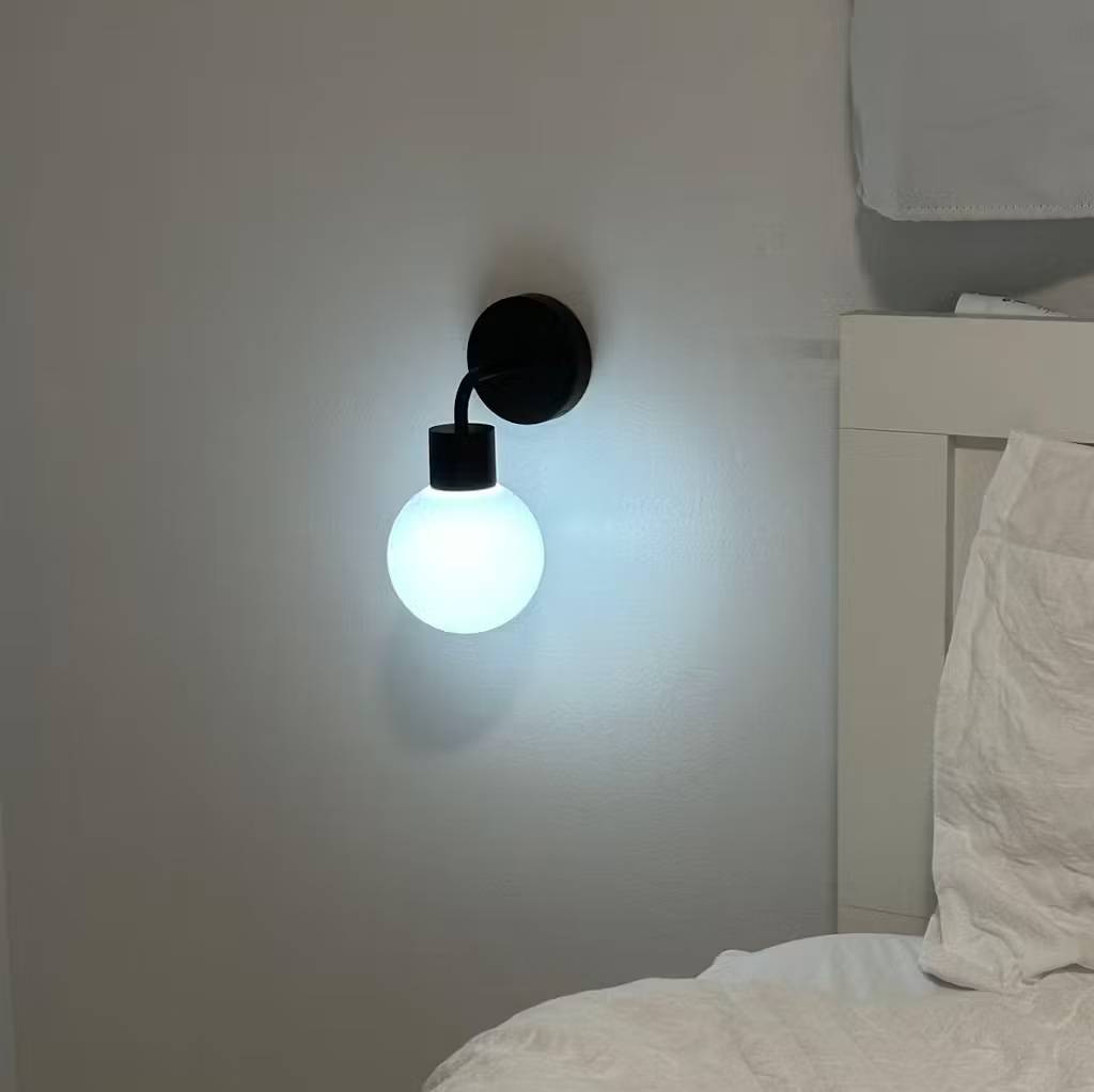 A glowing wall sconce above a white bed in a minimalist bedroom.