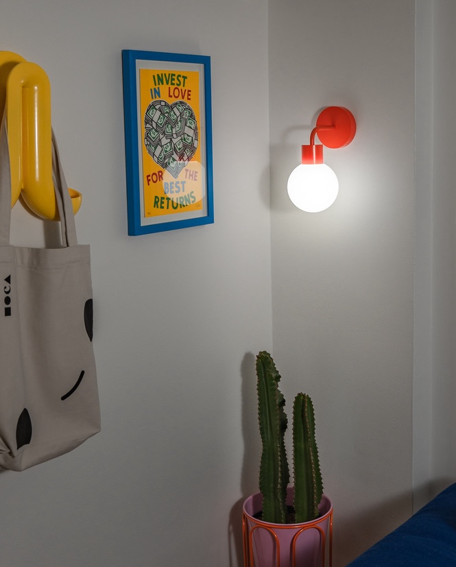 A cactus in a pot, wall art, and a wall lamp.