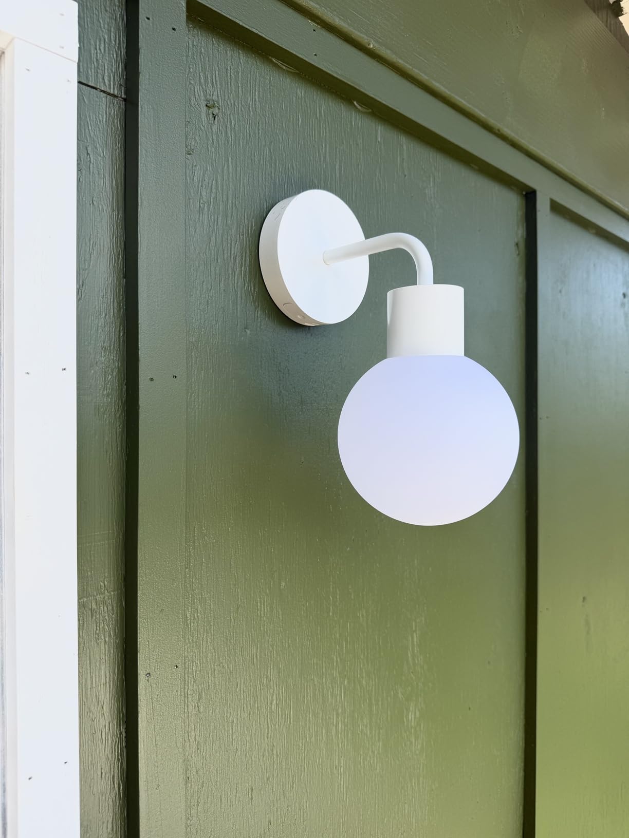 White round wall light fixture on a green wooden exterior.