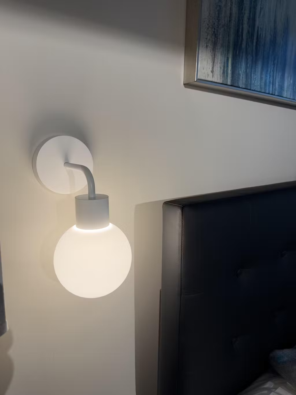 Wall-mounted lamp next to a black headboard and abstract painting.